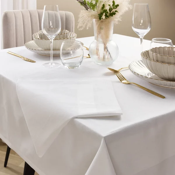 A Hotel Pure Luxury satin band napkin sat on a table that's set with wine glasses, plates and cutlery. There is a vase of flowers in the centre of the table.