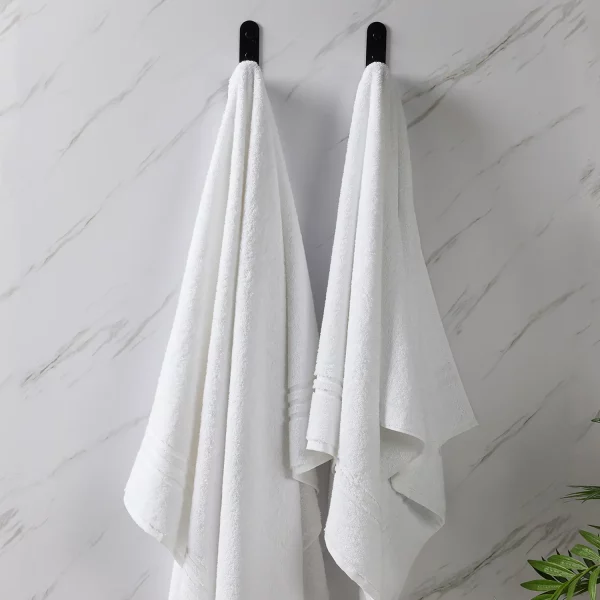 Two Hotel Pure Luxury signature towels hanging from hooks on a bathroom wall.
