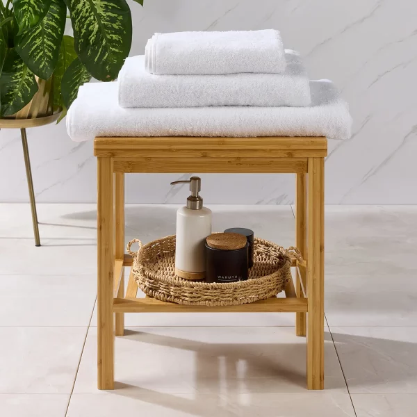Three Hotel Pure Luxury Classic towels sitting on a table. Underneath is a soap bottle dispenser with some pots in a basket. The towels include a bath sheet on the bottom, a bath towel in the middle and a hand towel on the top.