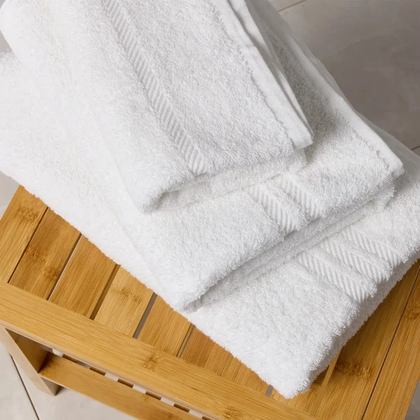 A stack of Hotel Pure Luxury Premier towels on a wooden table in a bathroom. There is a white hand towel, bath towel and bath sheet pictured.