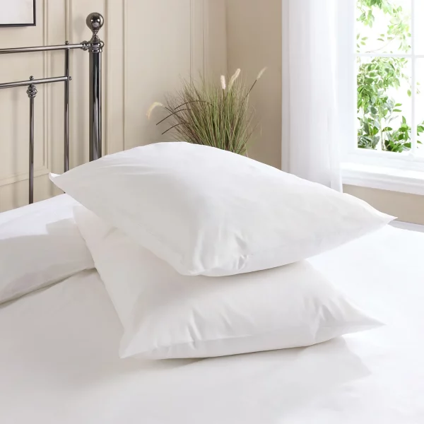 Hotel Pure Luxury cotton percale pillowcases covering two pillows that are sitting on a metal framed bed. A window is visible in the background, as is the top of a plant that's sitting on the floor.