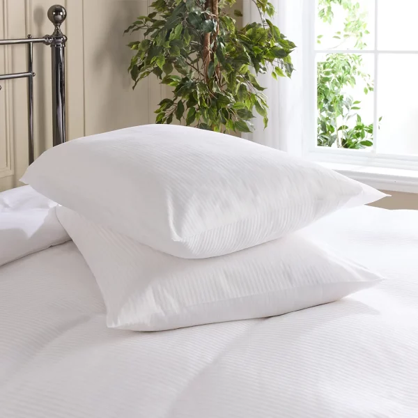 Hotel Pure Luxury cotton percale satin stripe pillowcases covering pillows that are sitting on a bed. There is a plant and window visible in the background.