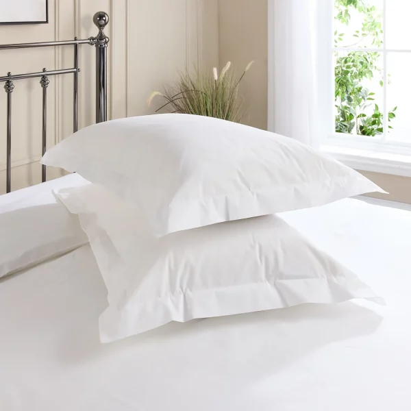 Hotel Pure Luxury cotton rich oxford percale pillowcases covering two pillows that are sitting on a metal framed bed. A window is visible in the background, as is the top of a plant that's sitting on the floor.
