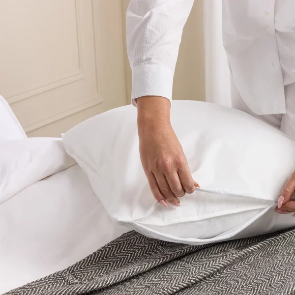 A woman putting a Hotel Pure Luxury waterproof anti-allergy pillow protector on a pillow.