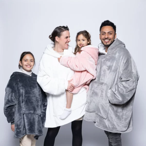 A family wearing Hudi wearable blankets. The adult female is wearing a cream Hudi whereas the adult male is wearing a silver Hudi. The two female children are wearing charcoal and pink Hudi's.