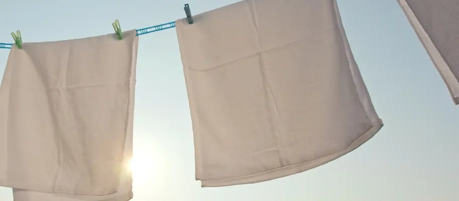 Linen hanging by pegs on a washing line outside, drying in the sun.