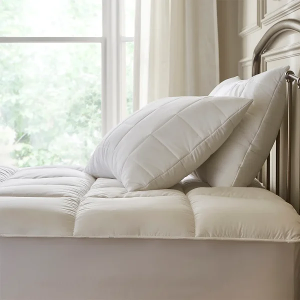 A white Hotel Pure Luxury Premium Suite Waterproof Mattress Topper & Pillow Protector Set on a bed. There is a window in the background.