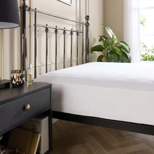 A close-up of a Hotel Pure Luxury 5 star 480 thread count white cotton fitted sheet on a metal framed bed.