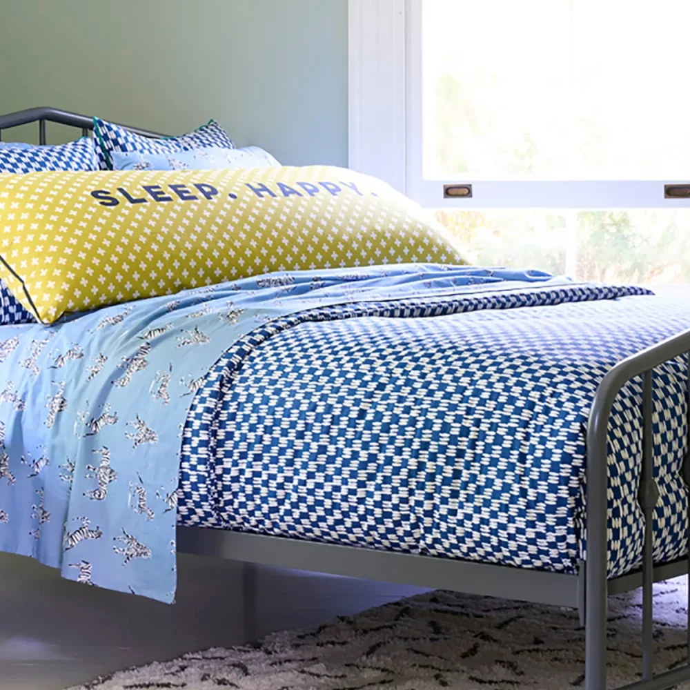 A painted blue check cotton duvet cover set with painted blue pillowcases. Also visible is a Zebras in Love fitted sheet and Sleep Happy body pillow, both of which are available separately.