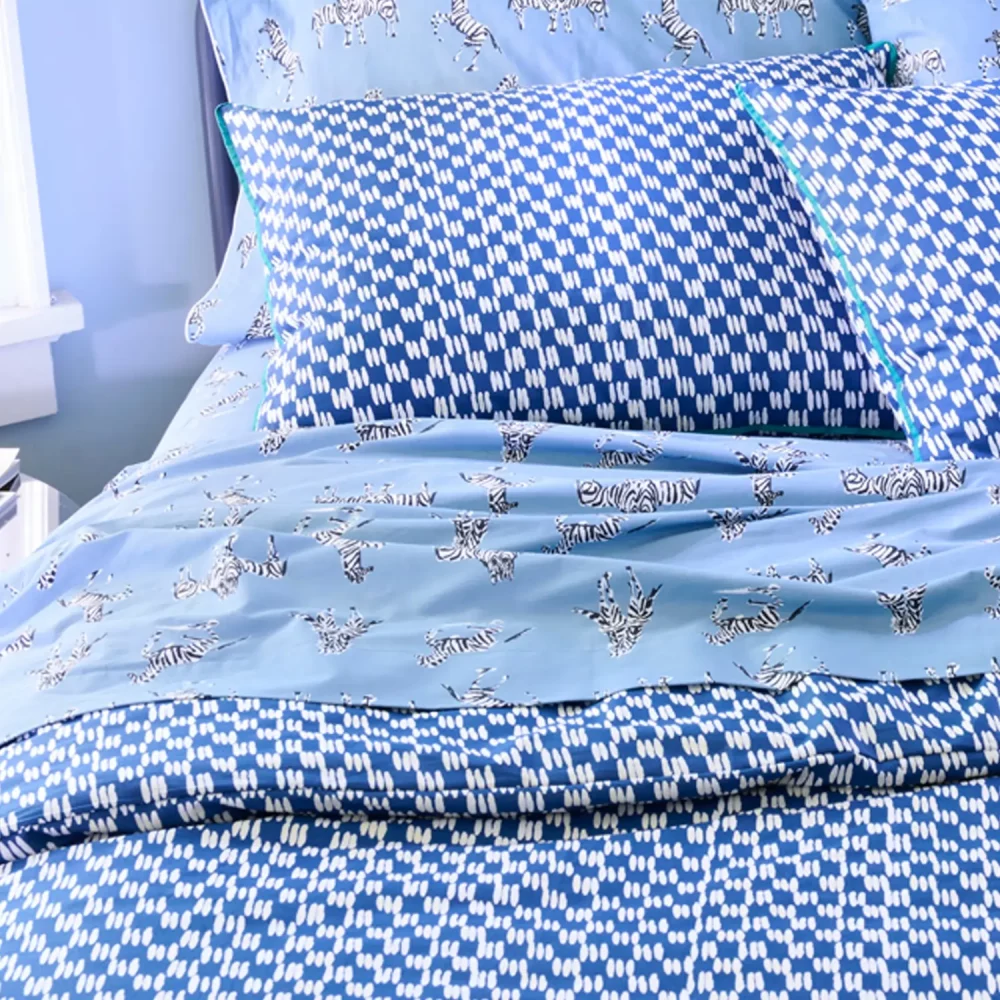 A closer view of a painted blue check duvet cover set with painted blue pillowcases. Also visible is a Zebras in Love fitted sheet, available separately.