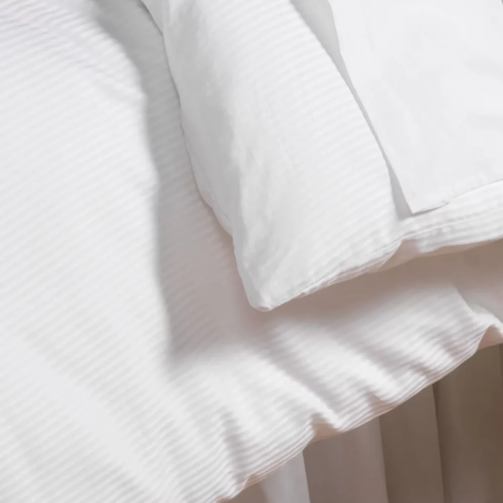 A close up of a 100% cotton white duvet cover with a 5mm satin stripe design. From Liddell.