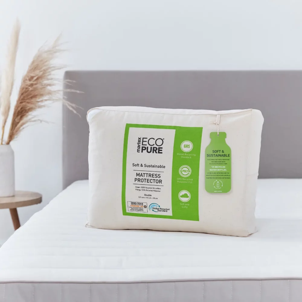 A package shot of the ecopure recycled 100% microfibre mattress protector. The package is white and green and is sitting on top of one of the protectors that's on a bed