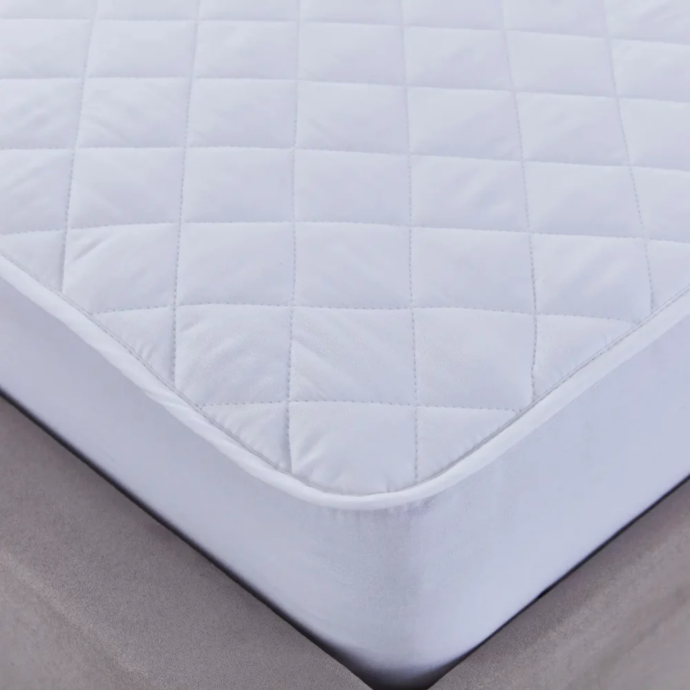 A close up of a Martex 100% cotton quilted mattress protector sitting on a mattress.