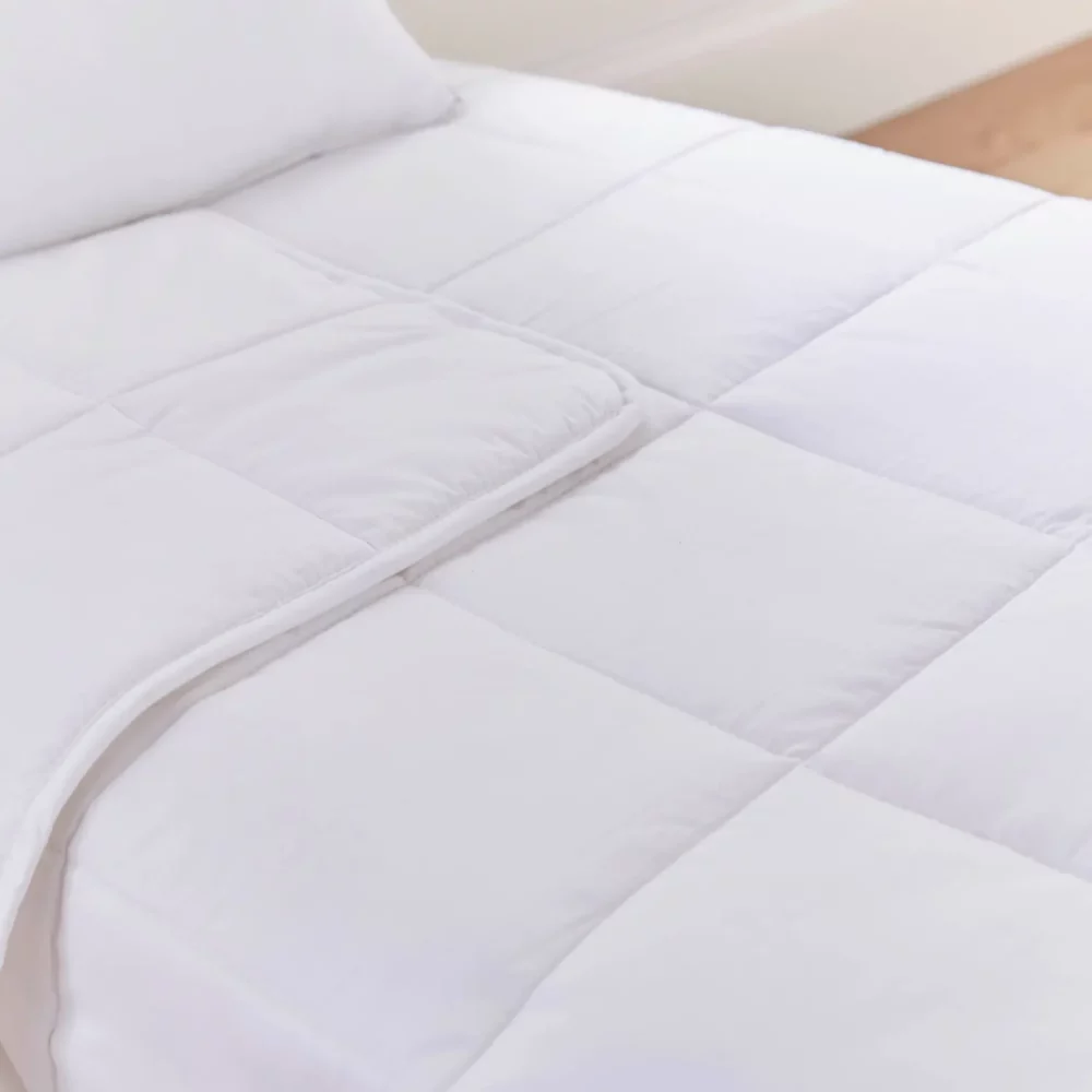 A close up look at a white temperature regulating 4 tog cot bed duvet from Martex Baby. The duvet has a square grid design. The duvet is slightly folded back.