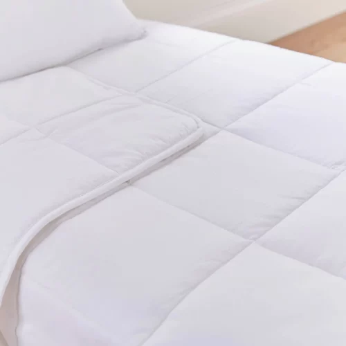 A close up look at a white temperature regulating 4 tog cot bed duvet from Martex Baby. The duvet has a square grid design. The duvet is slightly folded back.