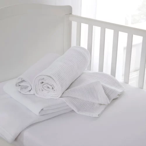 A white cot bed starter set from Clair De Lune sitting in a cot. It contains a fitted sheet, cellular blanket, and polar fleece blanket.