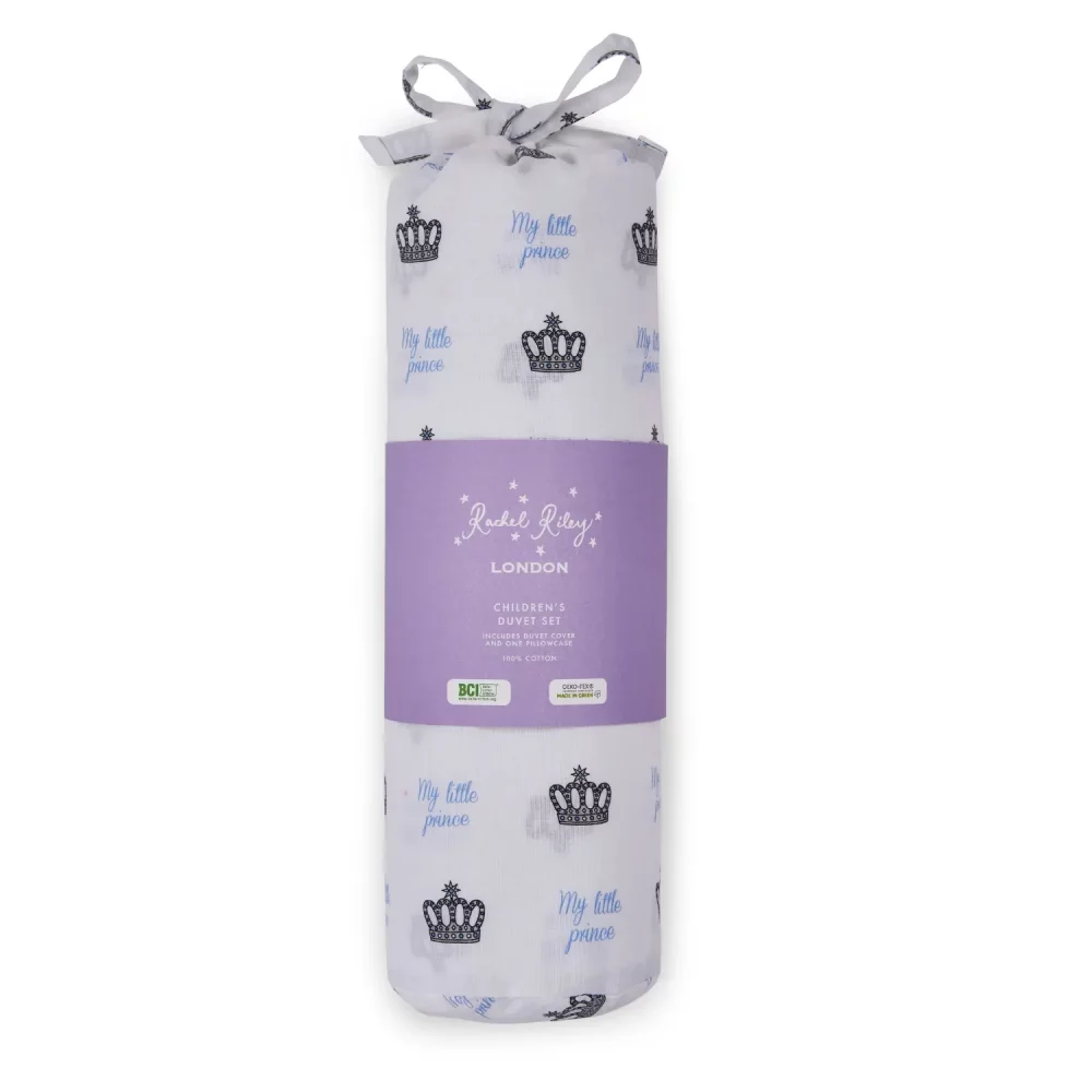 A white duvet cover and pillowcase set from Rachel Riley in its packaging. It comes in a bag which features a print of small crowns all across it with blue writing that says 'My Little Prince'.