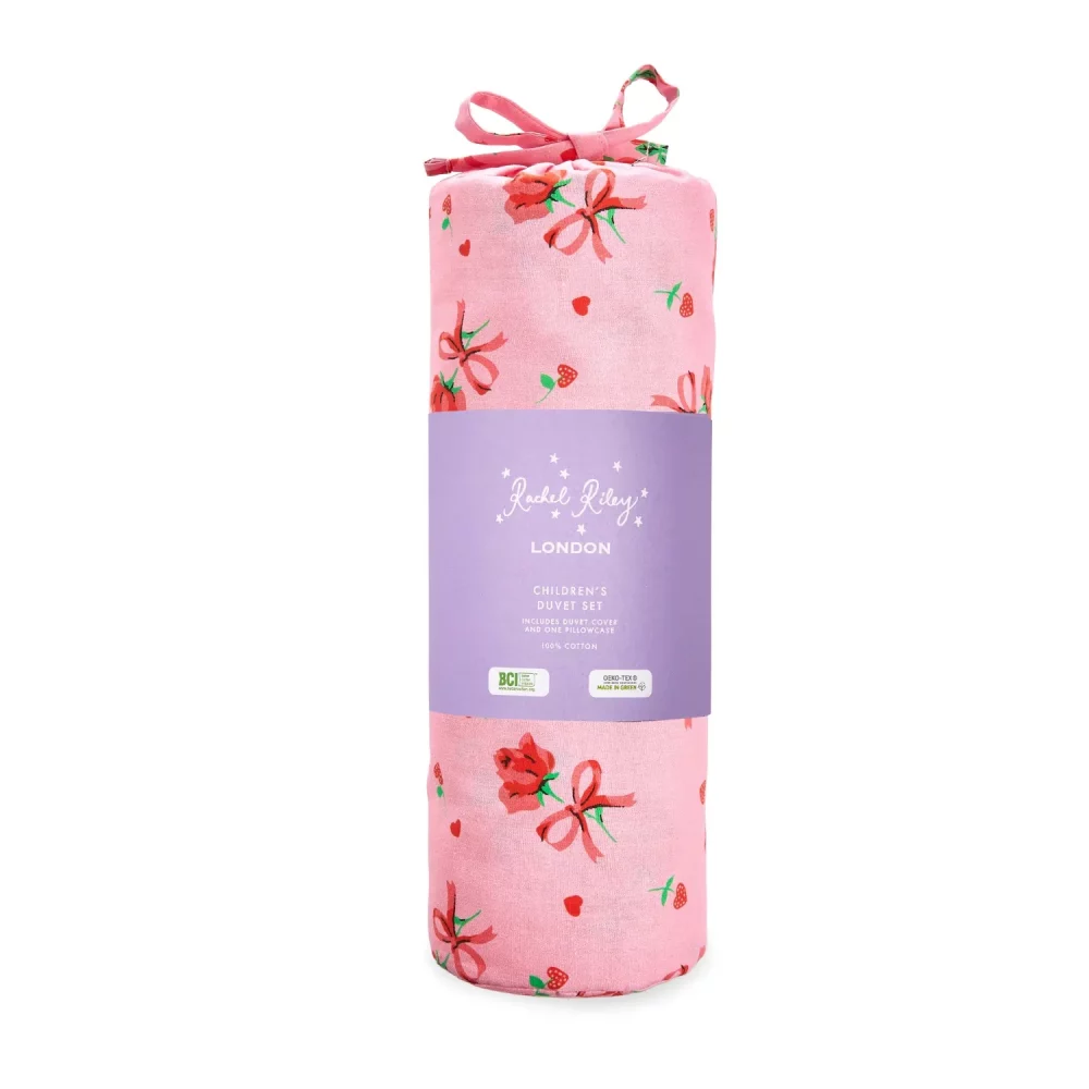 A pink strawberry rose duvet cover and pillowcase set from Rachel Riley. The pattern includes roses with a red bow tied underneath them, and small red love hearts. It's in the packaging bag it comes in, with a red bow tying it off.