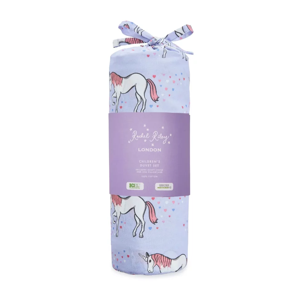 A lilac unicorn patterned duvet cover and pillowcase set from Rachel Riley. It's shown here its packaging bag, which is tied off with a bow.