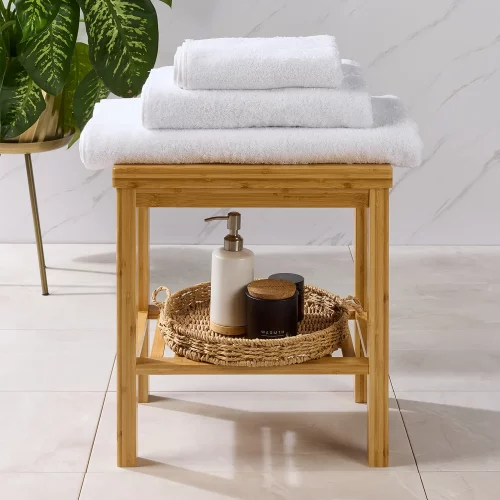 Three Hotel Pure Luxury Classic towels sitting on a table. Underneath is a soap bottle dispenser with some pots in a basket. The towels include a bath sheet on the bottom, a bath towel in the middle and a hand towel on the top.