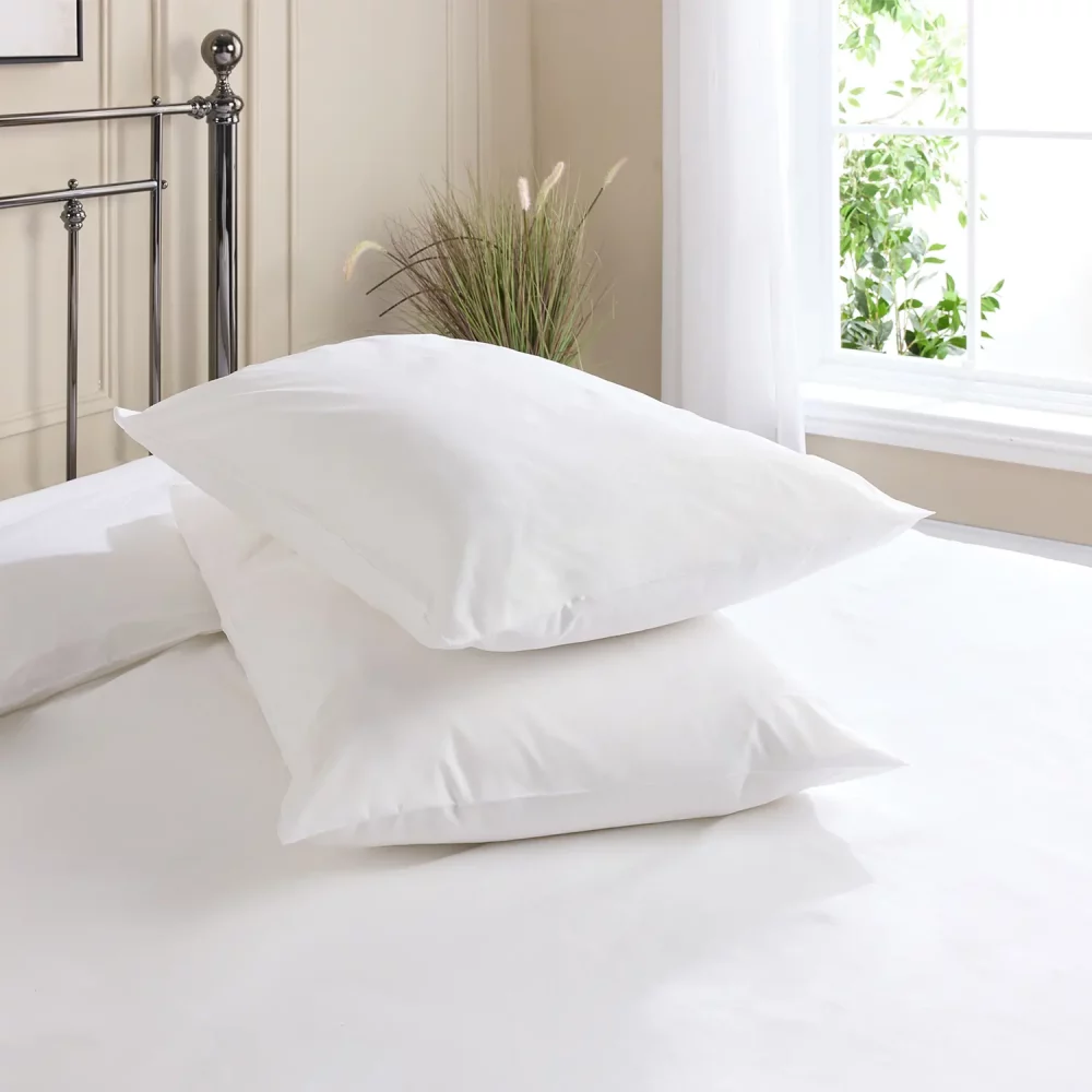 Hotel Pure Luxury cotton rich bag style percale pillowcases covering two pillows that are sitting on a metal framed bed. A window is visible in the background, as is the top of a plant that's sitting on the floor.