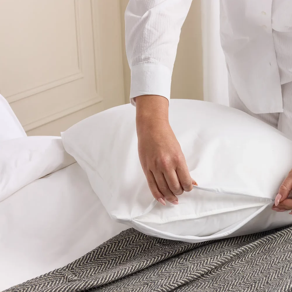 A woman putting a Hotel Pure Luxury waterproof anti-allergy pillow protector on a pillow.