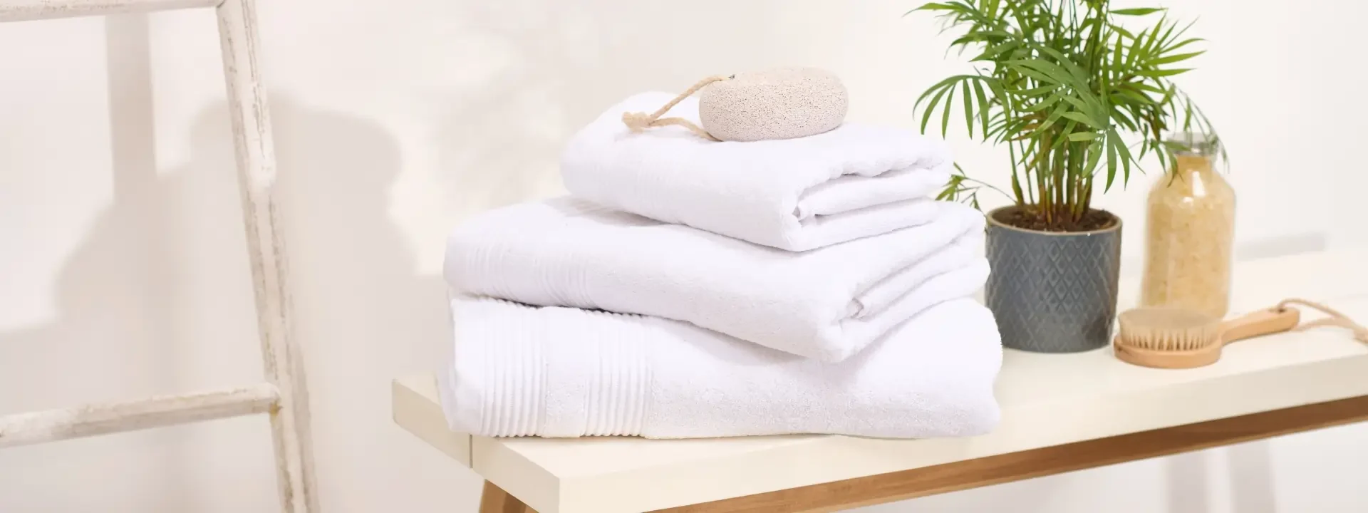 A stack of towels on a table with a plant, brush and bottle.